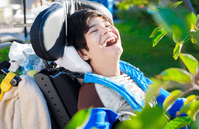 Young adult using a wheelchair smiling with greenery in the background.